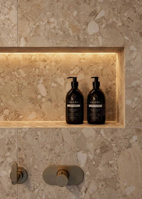 Modern bathroom with beige stone tiles and black soap dispensers in a niche.