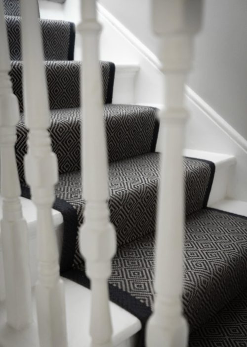Victorian staircase with black and white patterned carpet and white balustrades.