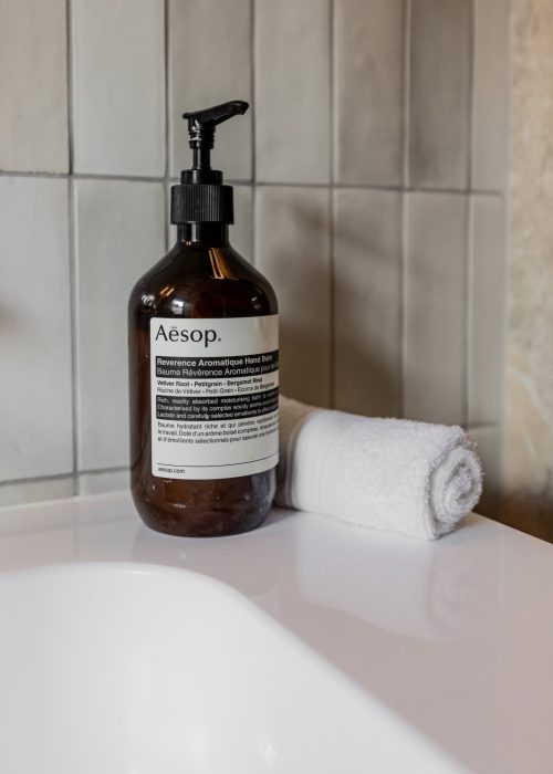 Aesop aromatic hand soap bottle with a rolled towel on a bathroom counter.