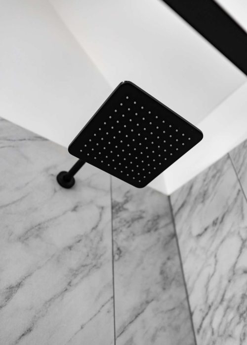Black square shower head with multiple small nozzles in a modern bathroom setting.