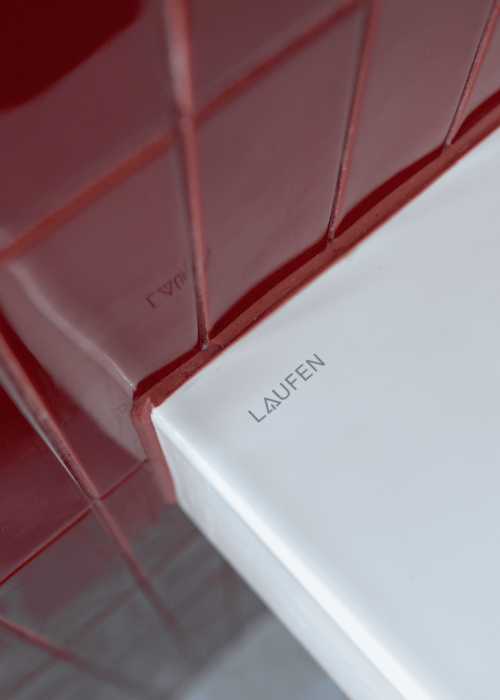 Close-up of a white bathroom sink with red tiled wall in a Victorian-style bathroom.