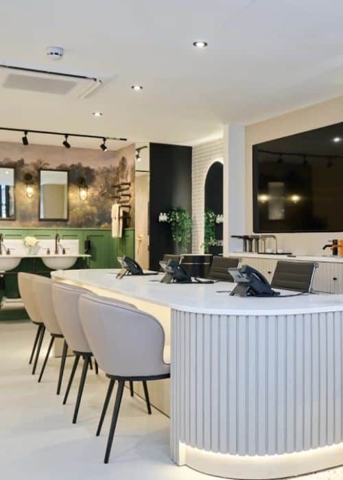 Modern bathroom showroom with sinks, seating, and a large TV display.