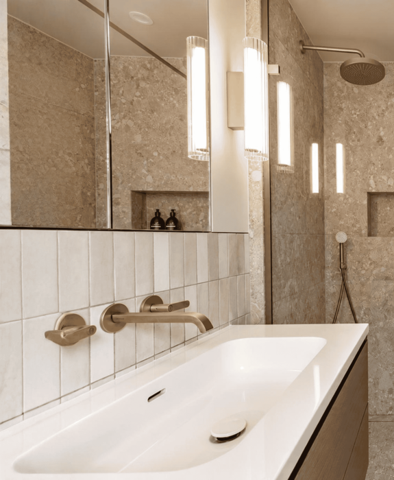 Modern bathroom with beige tiles, gold fixtures, and a white sink.
