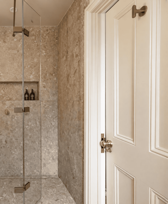 Modern bathroom with glass shower enclosure and beige stone tiles.