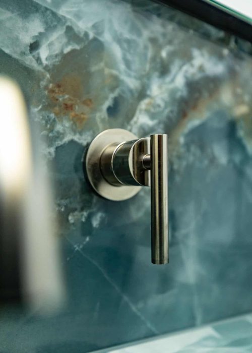 Close-up of a modern silver bathroom tap on a blue marble wall.