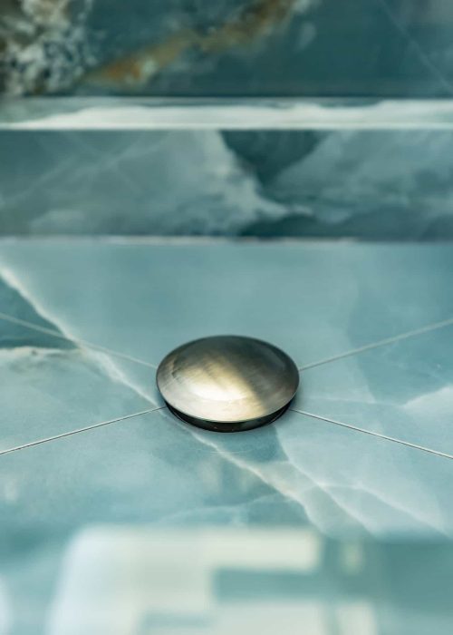 Close-up of a modern floor drain in a stylish bathroom with blue tiles.