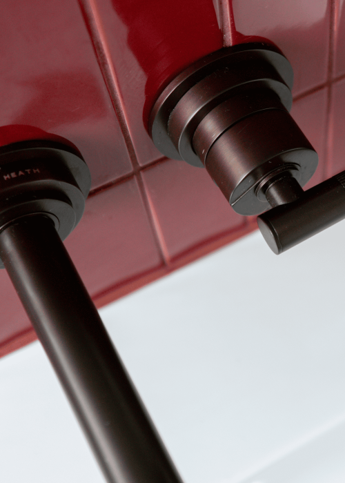 Close-up of black bathroom fixtures against red tiled wall in Victorian-style bathroom.