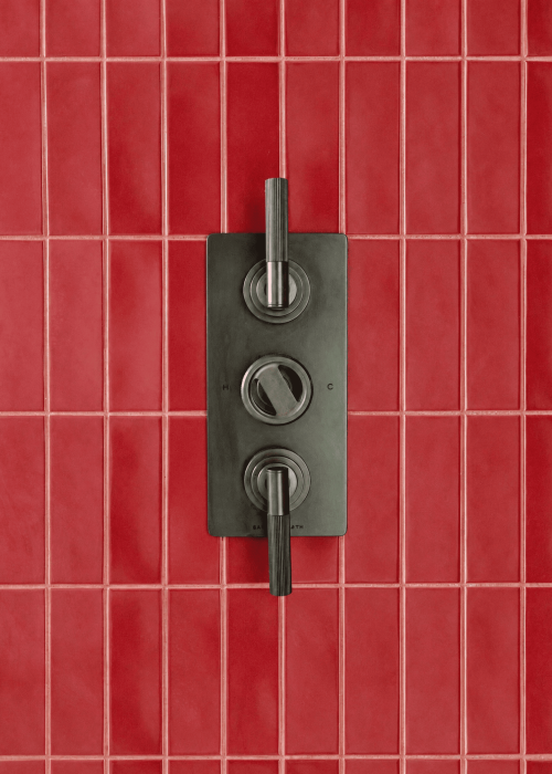 Close-up of vintage shower controls on red tiled bathroom wall.