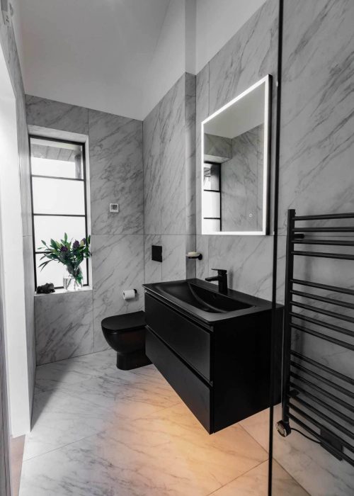 Modern black bathroom vanity with mirror and heated towel rail in marble-walled bathroom.
