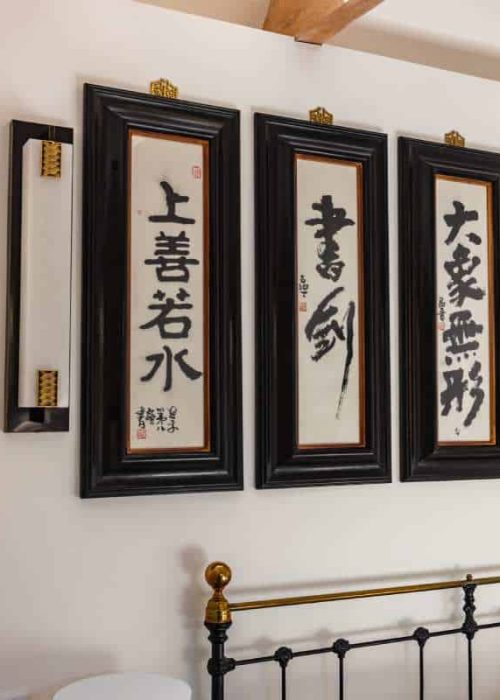 Decorative framed Asian calligraphy art on a white wall above a black metal bed frame.