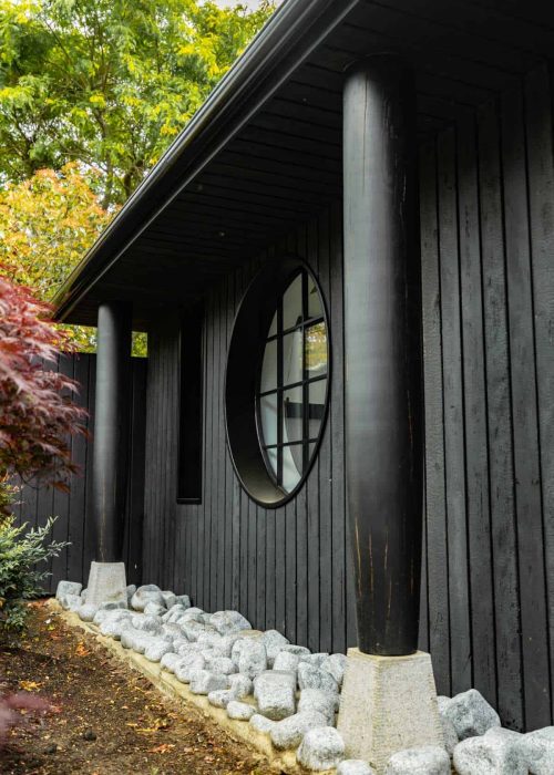 Modern black exterior with round window and stone landscaping.
