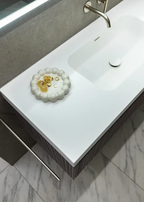 Modern white bathroom sink with decorative soap dish and grey wall background.